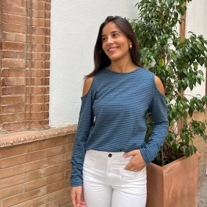 chica posando con una camiseta de rayas finas de color azul y gris antracita con los hombros descubiertos y mangas largas con un pantalón blanco