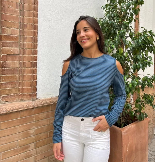 chica posando con una camiseta de rayas finas de color azul y gris antracita con los hombros descubiertos y mangas largas con un pantalón blanco