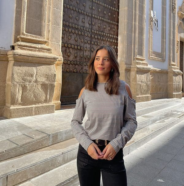 chica delante de una puerta de madera con una camiseta de rayas antracita rosa claro con hombros descubiertos y pantalón negro