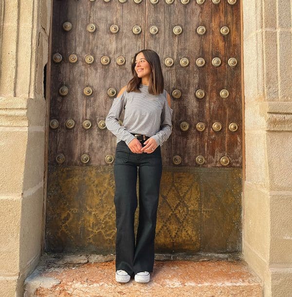 chica delante de una puerta de madera con una camiseta de rayas antracita rosa claro con hombros descubiertos y pantalón negro