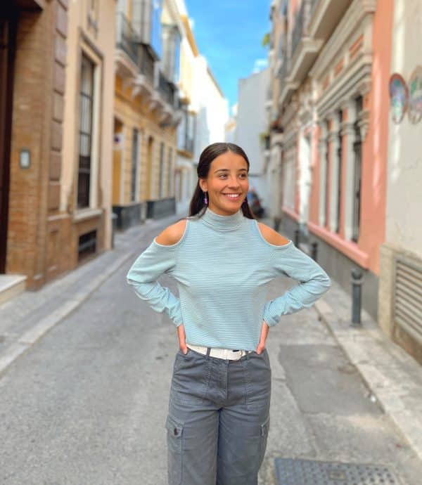 CHICA QUE VISTE CAMISETA VERDE AZULADO CON RAYAS FINAS BLANCAS. CUELLO VUELTO CON HOMBROS DESCUBIERTOS