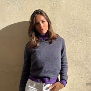 chica sobre una pared amarilla con jersey de cueloo vuelto de rayas moradas y verdes y patente en puños, cuello y bajo en morado