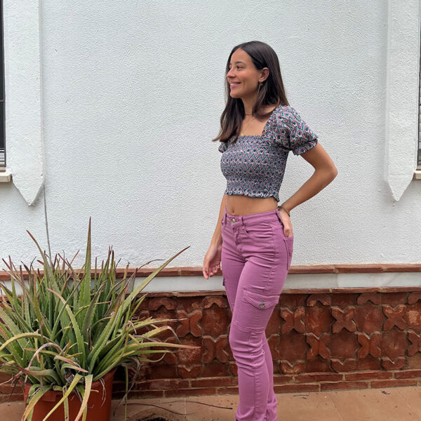 chica en un patio con un top fruncido corto estampado en color berenjena y verde sobre fondo blanco con mangas cortas y pantalón cargo rosa ajustado