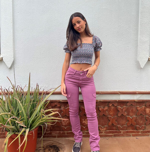 chica en un patio con un top fruncido corto estampado en color berenjena y verde sobre fondo blanco con mangas cortas y pantalón cargo rosa ajustado