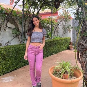 chica en un patio con un top fruncido corto estampado en color berenjena y verde sobre fondo blanco con mangas cortas y pantalón cargo rosa ajustado