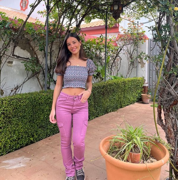 chica en un patio con un top fruncido corto estampado en color berenjena y verde sobre fondo blanco con mangas cortas y pantalón cargo rosa ajustado