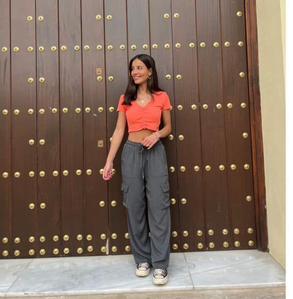 chica delante de una puerta de madera con un pantalón fluido gris antracita cargo y top naranja corto naranja con cordón frontal para fruncir