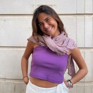 chica sonriendo con manos en os bolsillos con un pañuelo rosa viejo y top morado