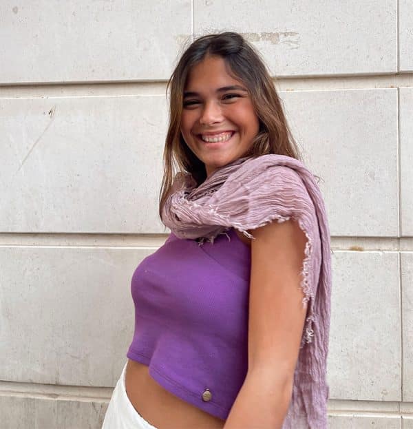 chica sonriendo con manos en os bolsillos con un pañuelo rosa viejo y top morado