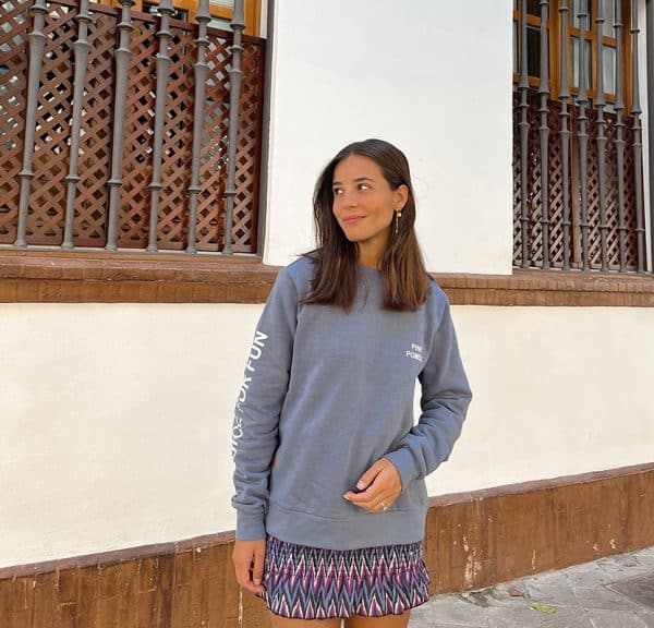 chica sonriendo con una sudadera azul con print crudo en pecho izquierdo y brazo derecho