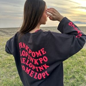 chica en la playa con una sudadera oversize en gris antracita con texto pinkpomelo en ondas en color coral flúor en espalda y manga derecha