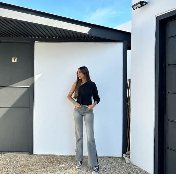 chica delante de una pared blanca con un top asimétrico negro de manga francesa abullonada con lurex dorado y pantalón gris con tachuelas