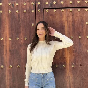 chica posando en la calle delante de un portal de madera con un top beige y un vaquerpo azul con tachuelas