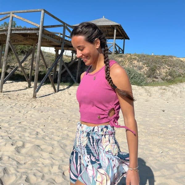 chica sonriendo en en la playa con un top fucsia y un short de flores