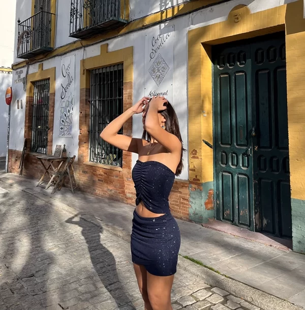 chica de perfil delante de una puerta de madera verde con las dos malos en el pelo con un conjunto azul de brillo de falda corta y top banda