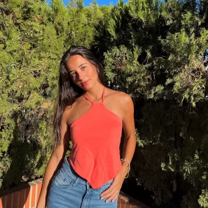 chica delante de una arbusto verde con un top pañuelo cuello halter en coral y pantalón tejano azul