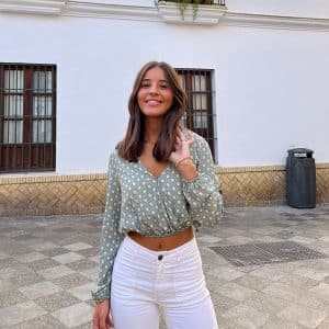 chica sonriendo con la mano en el pelo con pantalón blanco y blusa corta cruzada de manga larga verde con print blanco y verde