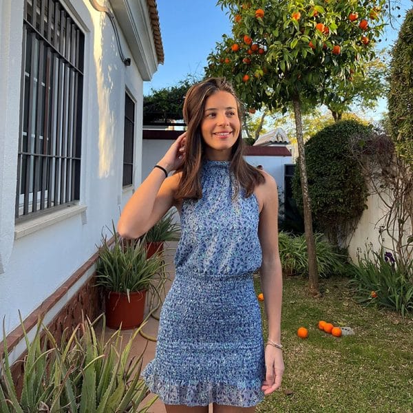 chica sonriendo en un jardín con vestido corto con gasa estampada azul con cuello halter y espalda descubierta con la parte de la falda fruncida y forro interior