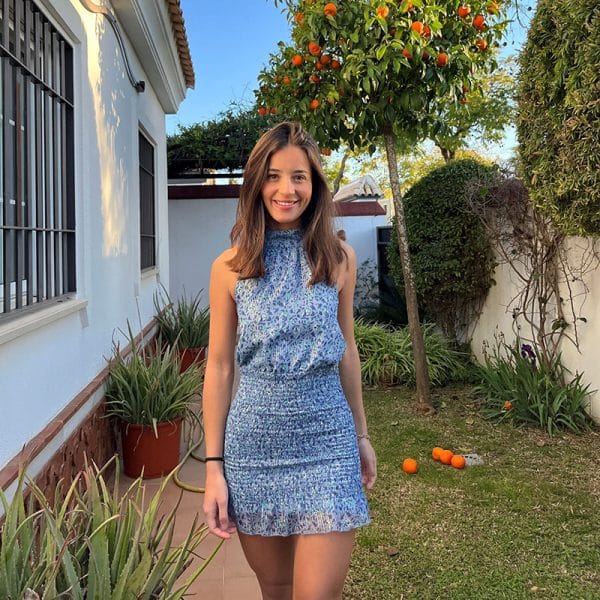 chica sonriendo en un jardín con vestido corto con gasa estampada azul con cuello halter y espalda descubierta con la parte de la falda fruncida y forro interior