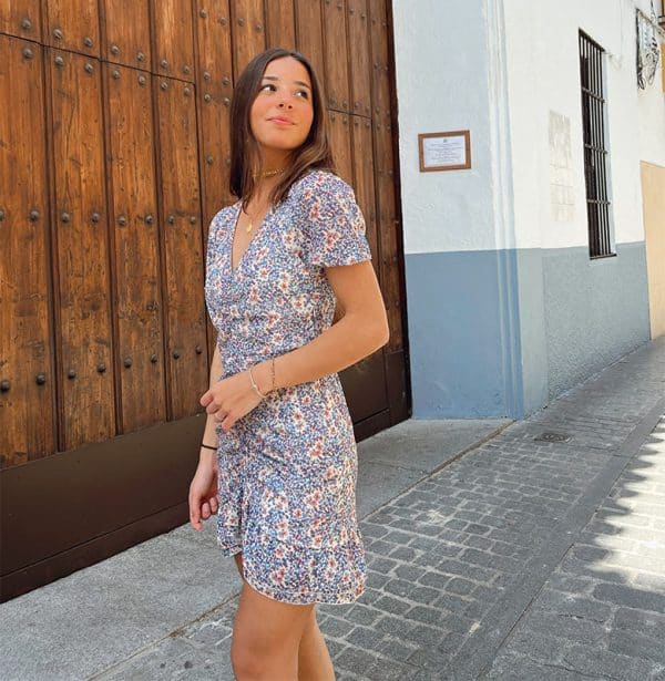 chica sonriendo con un vestido corto blanco con flores tonos azules fruncido en el centro y volante en bajo