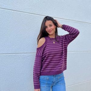 chica sonriendo delante de una pared blanca con un jersey de rayas morado con hilo de lúrex muy discreto en morado. Hombro derecho descubierto